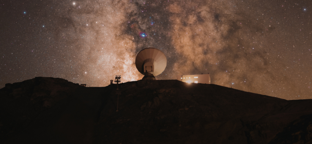 Astrobiologia e sinais potenciais de vida fora da Terra: quando a ciência aprende a procurar o impossível 4 Radiotelescópio em observatório astronômico sob o céu estrelado da Via Láctea, representando a busca por sinais de inteligência extraterrestre e observação do cosmos.