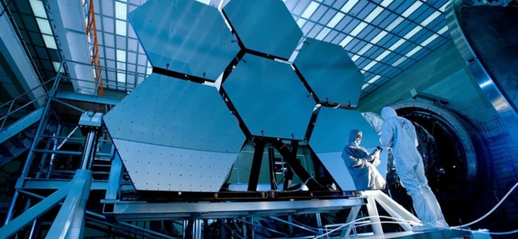 2026 - Telescópios espaciais: quando a humanidade decidiu enxergar além de si mesma 7 Esta imagem apresenta uma perspectiva fascinante dos bastidores da engenharia astronômica, mostrando parte do espelho primário do Telescópio Espacial James Webb (JWST) em um ambiente de laboratório.
