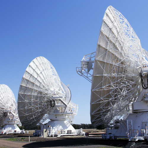 2026 - Telescópios espaciais: quando a humanidade decidiu enxergar além de si mesma 13 Telescópios espaciais: Os Equipamentos Estrutura: A imagem foca em três grandes antenas parabólicas (e parte de uma quarta ao fundo) pintadas de branco. Elas possuem uma estrutura complexa de treliças metálicas na parte traseira para suporte. Mobilidade: É possível notar que as bases dessas antenas estão montadas sobre trilhos ferroviários. Isso permite que os cientistas alterem a distância entre os telescópios, criando um interferômetro que funciona como um único telescópio gigante. Componentes: No centro das parábolas, há receptores sustentados por hastes, responsáveis por captar as ondas de rádio vindas do espaço.