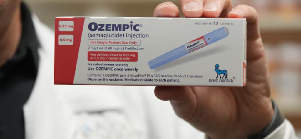 Mão segurando caixa de Ozempic injetável com informações de dosagem e fabricante em destaque.