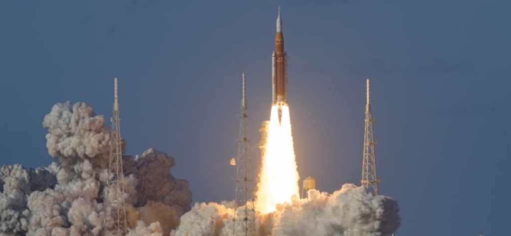 Lançamento do foguete SLS subindo ao céu com grande nuvem de fumaça para a missão Artemis ii.